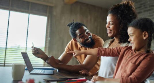 familiaux Happy African American family talking while using credit card for online shopping at home. Focus is on woman.