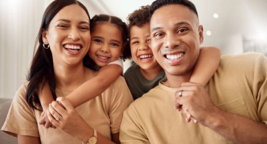Hug, children and parents on the sofa in the living room of house for love, care and happiness. Portrait of happy and young kids hugging mother and father with affection in the lounge of their home