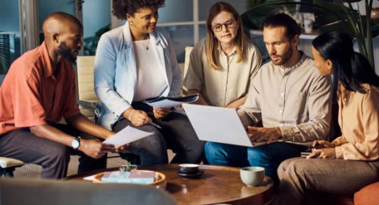 Group of five diverse businesspeople talking having a meeting using a laptop together at work