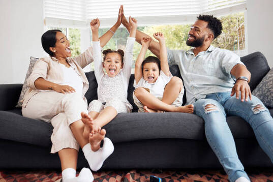 gestion-colere Happy parents and excited children celebrate on the sofa while watching television. Fun family time, relaxing at home and bonding. Mother and father high five, kids cheer for sports team win.