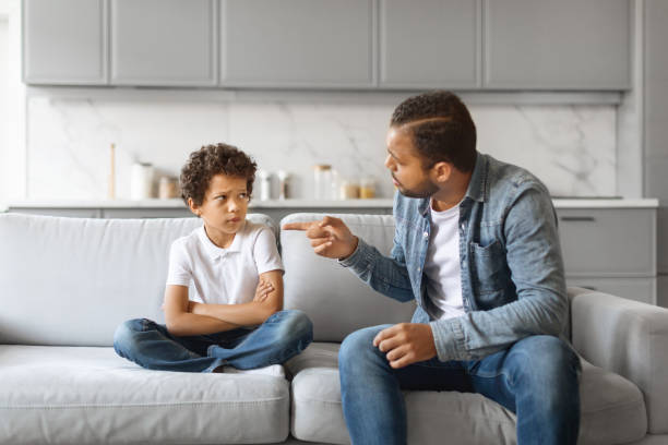 gestion_colere Angry african american father scolding upset little son at home, preteen black boy sitting on couch with arms crossed, dad and male kid having quarrel, suffering misunderstanding, closeup